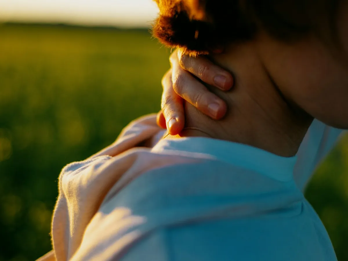 A woman holding her neck and shoulder in warm evening light