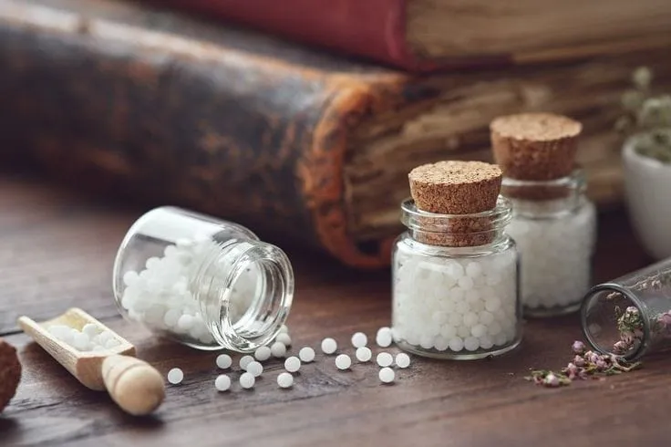 Open glass jars of homeopathy globules on a wooden table