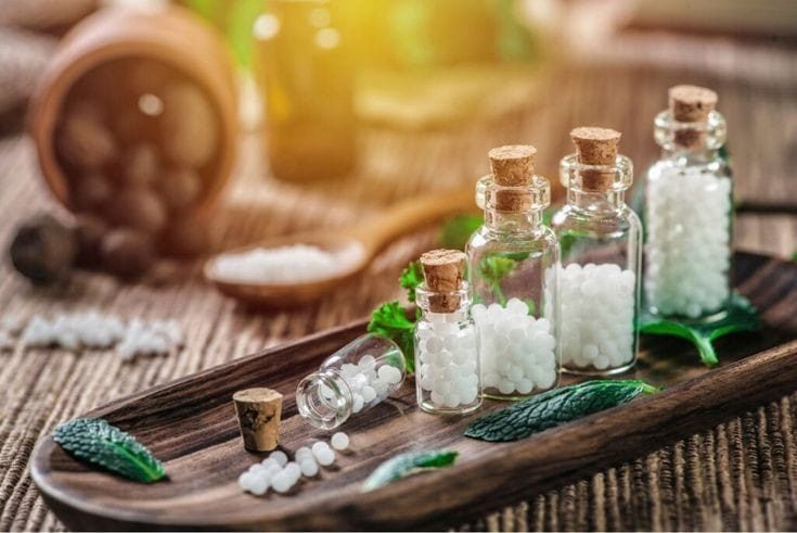 Small glass bottles of homeopathy globules on a wooden tray with fresh leaves