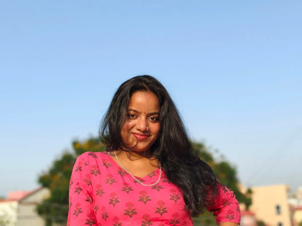 A young woman in a pink kurti smiling outdoors